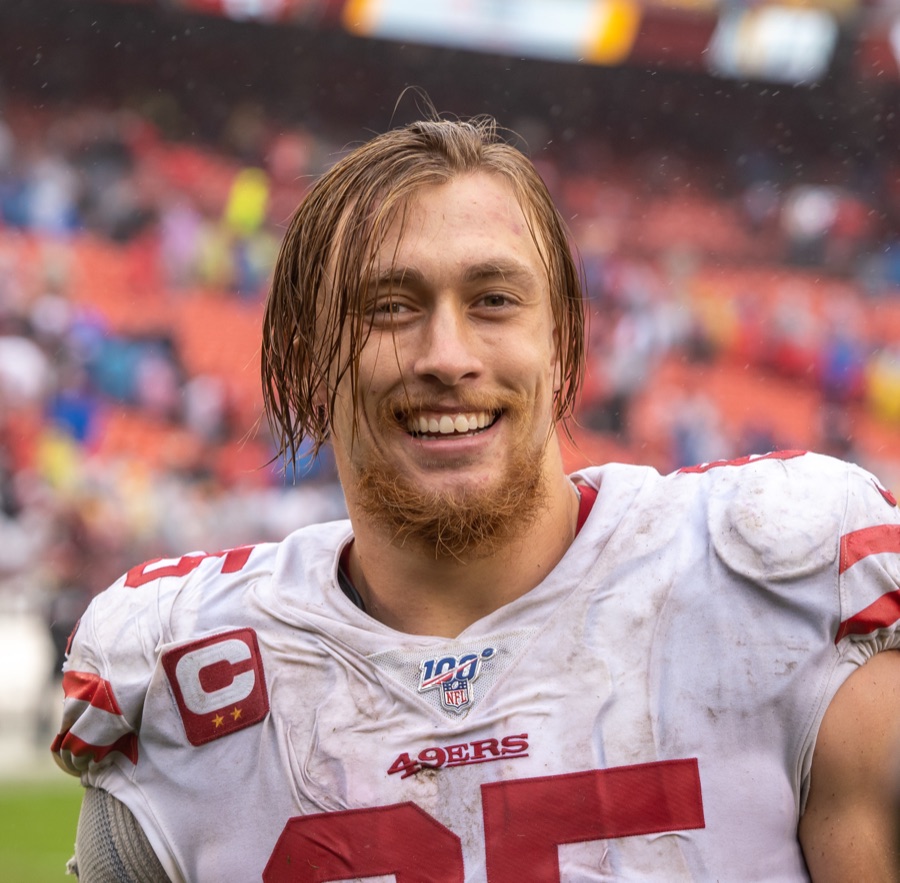 George Kittle in a muddy 49ers away jersey, smiling after a game